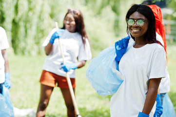 Naklejka premium Group of happy african volunteers with garbage bags cleaning area in park. Africa volunteering, charity, people and ecology concept.