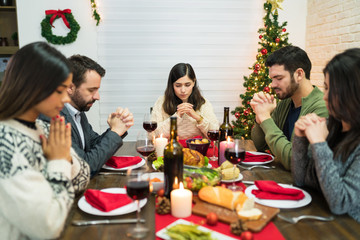 Men And Women Praying During Christmas Dinner At Home