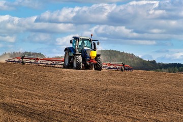 A blue tractor sows grain. Farm work on a farm in the Czech Republic. Tractor on a wheat field. Agricultural machinery.