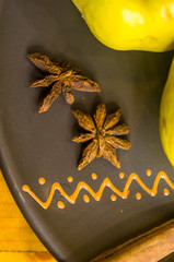 Star anise spice fruit and fruits of yellow quince on a brown ceramic plate with ornament, macro
