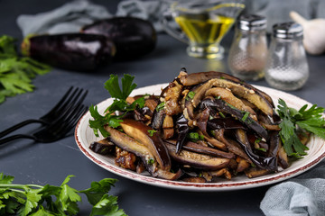 Fried eggplants with garlic and soy sauce, sliced in stripes, in a plate against a dark background