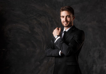 Young man in a black suit on a gray background. Bearded businessman smiling