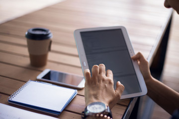 Women's hands with neat manicure and large wristwatch, work with gadgets, tablet, smartphone, papers on a wooden table.