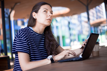 Close-up, portrait of a serious, gently smiling girl student, freelancer, blogger working at a...