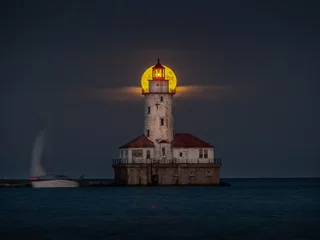  A beautiful night shot of the harvest full moon as it aligns with the center top of the abandoned historic light house tower along Lake Michigan in Chicago as sailboat passes by on the dark water. © Joseph Kirsch