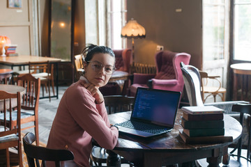 Site development. Smart girl with a soft smile, sits at desk in the library, in front of her is...