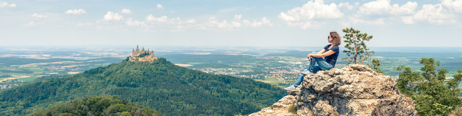 Landscape with young woman and Hohenzollern Castle, Germany. Adult girl travels in Alpine mountains...