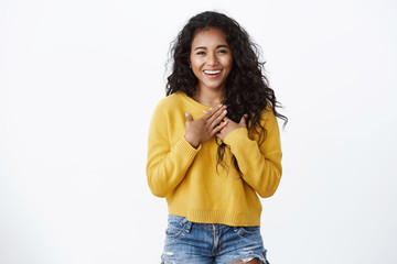 Pleased and flattered cute smiling african american curly-haired girl, wear yellow cozy sweater, press hands to chest, feeling grateful thanking for help, grinning appreciate lovely gift
