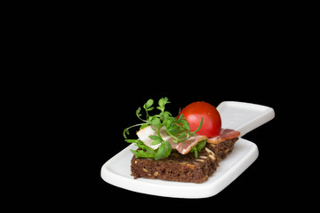 Sandwich with bacon, tomatoes and herbs on a black background, dark key.