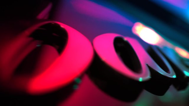 Bar signboard on defocused smooth dark wall under multicolor muffled light. Golden letters, a title on a party with bokeh effect at evening time, close-up. 