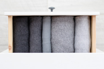 knitted women's winter clothes in shades of gray from light to dark neatly folded in an open drawer