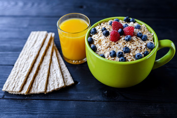 Healthy breakfast: oatmeal with berries and a glass of fresh juice on a dark wooden table.