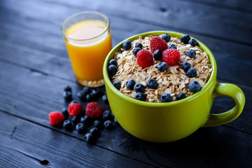 Healthy breakfast: oatmeal with berries and a glass of fresh juice on a dark wooden table.