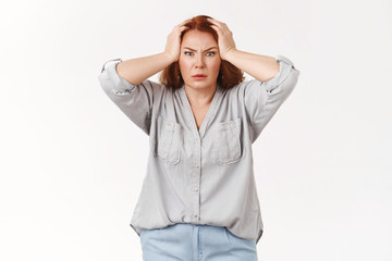 What disaster. Shocked panic redhead woman grab head troubled frowning bothered feel pressured distress facing trouble terrible scene displeased huge mess kids made, standing white background