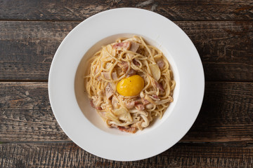 spaghetti carbonara with a yolk on top, white round serving dish and wood background