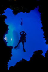 A shot of a scuba diver taken through a window in the coral reef. The silhouette of a dive boat can be seen floating on the surface way above