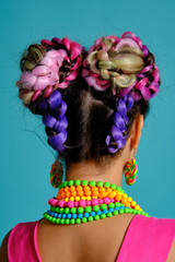 Lovely girl with a multi-colored braids hairstyle and bright make-up, posing in studio against a blue background.