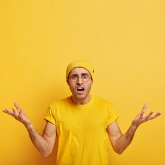 Indignant puzzled young man raises arms with annoyance, feels doubtful, faces difficult situation,...