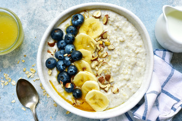 Oatmeal porridge with banana, fresh blueberry and nuts - healthy breakfast. Top view with copy space.