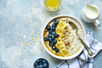 Oatmeal porridge with banana, fresh blueberry and nuts - healthy breakfast. Top view with copy space.
