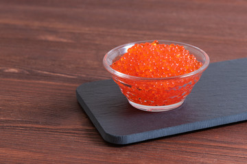 Red caviar in the glass jar on the dark brown wooden background