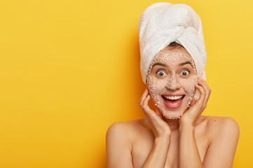 Joyful adorable woman with glad facial expression, applies natural sea salt mask, has healthy well...