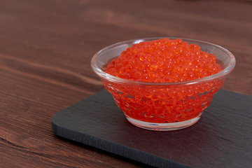 Red caviar in the glass jar on the dark brown wooden background