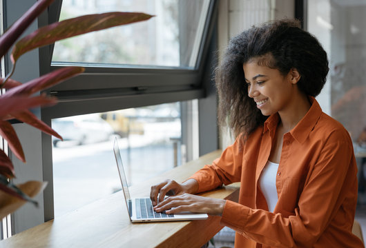 Happy African American woman copywriter working freelance project in modern cafe. Businesswoman using laptop, searching information on website. Successful business. Online training courses concept