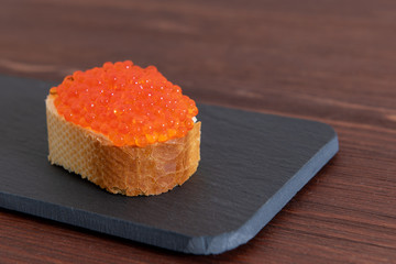 Red caviar with white bread on the dark brown wooden background