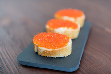 Set of three sandwiches with red caviar on the grey stone background