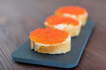 Set of three sandwiches with red caviar on the grey stone background