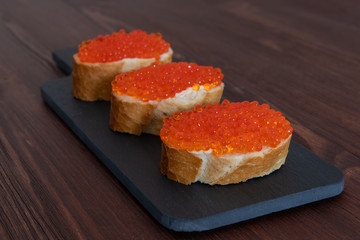 Set of three sandwiches with red caviar on the grey stone background