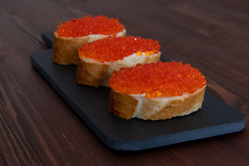 Set of three sandwiches with red caviar on the grey stone background