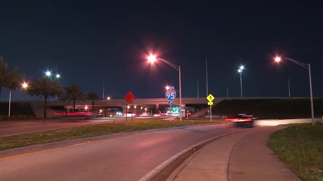 Traffic Moves Past and By Three Signs, Truck Entering and Leaving Highway, I-95 with Arrow and Pedestrians Crossing, in a Slow Shutter-Speed Time-Lapse from Sample Road Pompano Beach, Florida at Night
