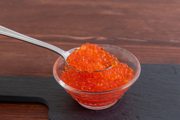 Fototapeta na wymiar Red caviar in glass jar with silver spoon on the dark brown wooden background