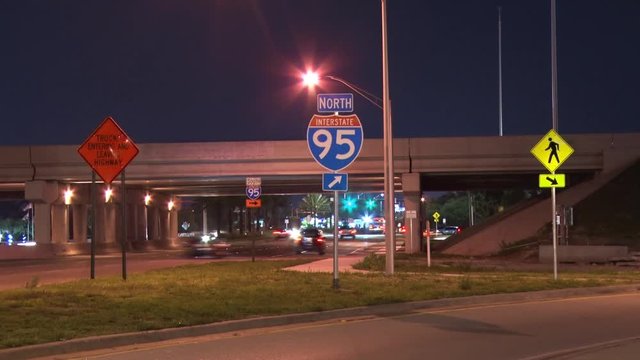 Traffic Moves Past and By Three Signs, Truck Entering and Leaving Highway, I-95 with Arrow and Pedestrians Crossing, in a Slow Shutter-Speed Time-Lapse from Sample Road Pompano Beach, Florida at Night