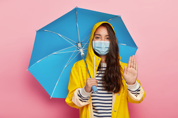 Serious girl makes stop gesture, asks not pollute environment, walks in acid rain, wears protective...