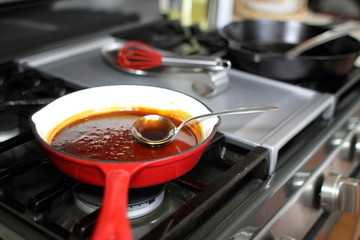 Demi-glace cooked in a coated enamel skillet on the stove top in a home kitchen.