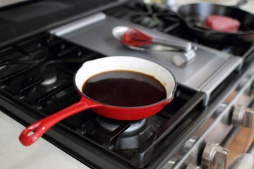Demi-glace cooked in a coated enamel skillet on the stove top in a home kitchen.