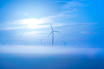 Sun shines on wind turbines in a foggy field at sunrise in summer