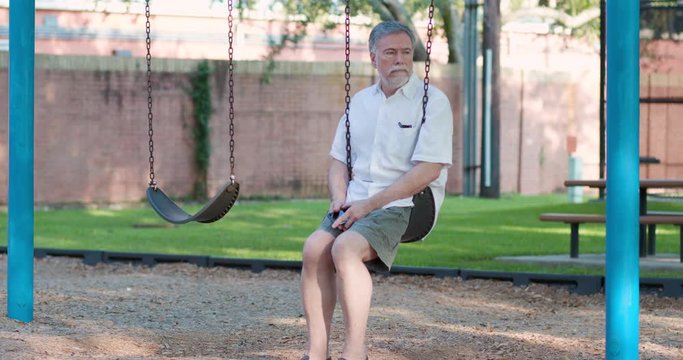 A melancholy mature widower sits alone on a playground swing.