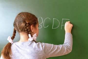 Elementary school girl stands in front of a blackboard and writes with chalk