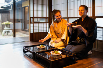 Couple in kimono seiza sitting, holding chopsticks, eating food at traditional Japanese home ryokan...