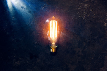 Vintage old light bulb glowing yellow on rough dark background. Idea, creativity concept.