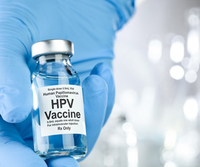Healthcare concept with a hand in blue medical gloves holding HPV, human papillomavirus, vaccine vial