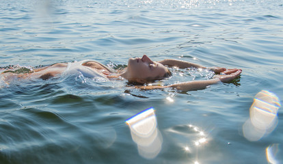 Relaxing on beach resort. Beautiful woman is swimming on back in sea.