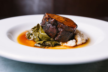 Glazed pork shoulder dish with greens and creamy mashed hominy served on white plate