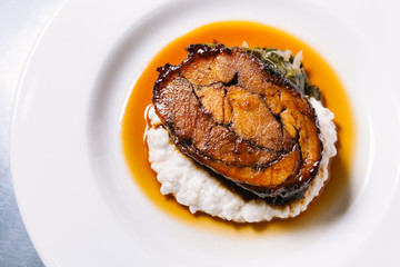 Glazed pork shoulder dish with greens and creamy mashed hominy served on white plate