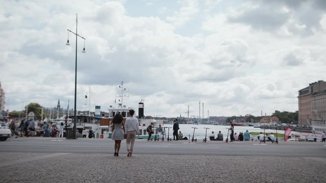 Wide shot of a young travelling couple strolling and holding hands in a harbour in Stockholm.
