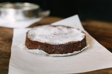Traditional lumberjack fruit cake dusted with powdered sugar on parchment baking paper on wood surface with sheet pan in background